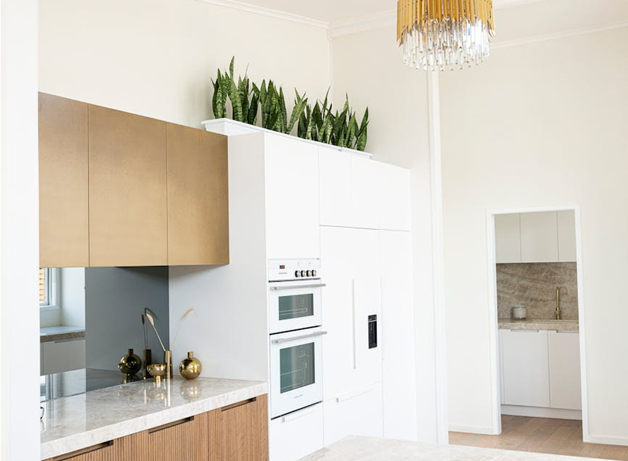 Premium Stones enhance this modern kitchen with elegant white cabinets, golden accents, and a sleek marble countertop.