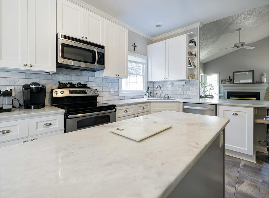 Premium Stones elevate this modern kitchen with white cabinets, stainless steel appliances, and a marble island.