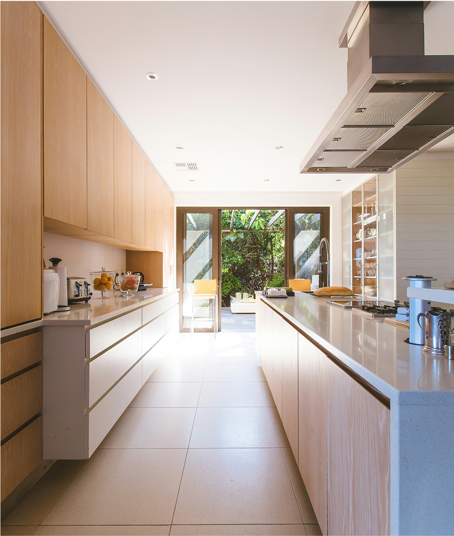 A bright and spacious modern kitchen with wooden cabinets, white countertops, and large glass doors leading to an outdoor space.